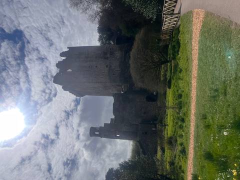       Silhouetted medieval tower of Blarney Castle rises beneath bright midday sun and patchy clouds.
  