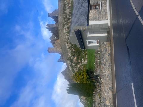       Distant ruined hilltop fort seen beyond village buildings and wet roadside.
  
