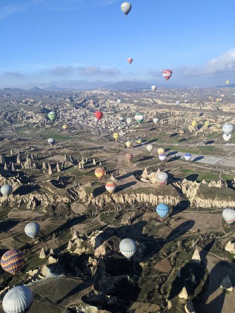       Wide aerial landscape of Cappadocia’s valleys filled with colorful hot-air balloons drifting above unique rock formations.
  