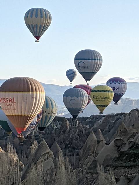      Zoomed-in shot of several hot-air balloons floating above rugged rocky cliffs in Cappadocia.
  
