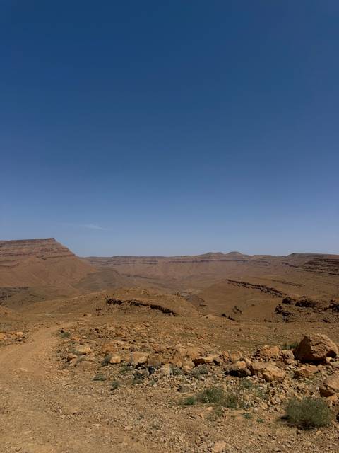       Wide open arid mountain range and barren brown ridges beneath a cloudless blue sky.
  
