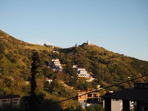       Hillside dotted with white buildings and a small summit shrine under late afternoon light.
  