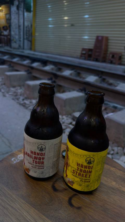       Close-up of two cold beer bottles resting on a narrow table beside railway tracks
  