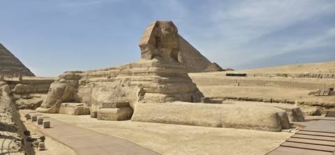       Side view of the Great Sphinx of Giza with desert plateau and a pyramid behind
  