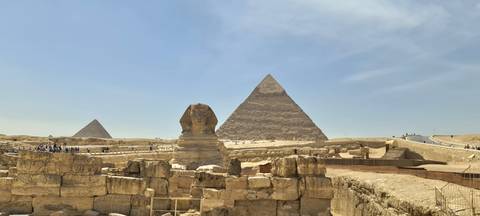       Great Sphinx with two pyramids rising behind framed against clear desert sky
  
