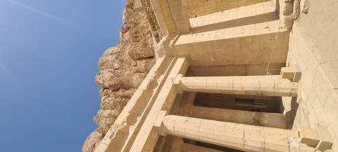       Massive rock backdrop towers above the colonnaded entrance of Hatshepsut Temple under blue sky
  