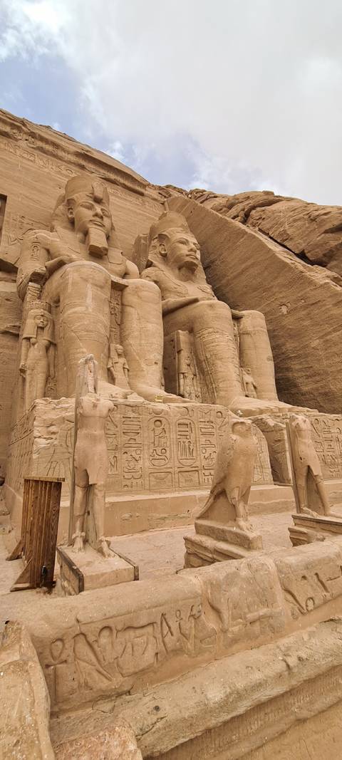      Close details of seated pharaoh statues and hieroglyphs carved into the sandstone facade of Abu Simbel
  