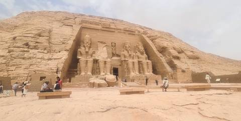       Wide view of Abu Simbel rock temple with scattered visitors across sandy forecourt
  