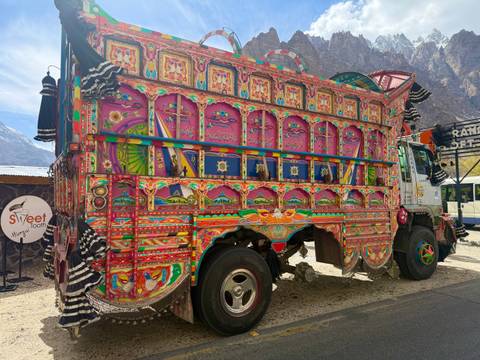       Vibrantly painted Pakistani truck adorned with intricate floral and geometric designs parked in a mountainous area.
  