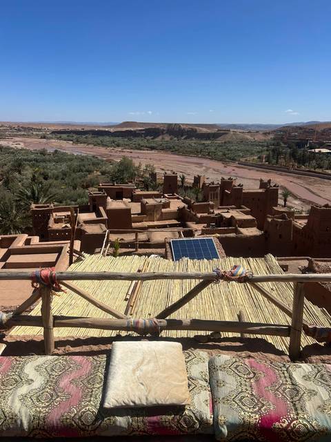       Elevated view over the mud-brick kasbah buildings of Ait Benhaddou and a dry riverbed beyond.
  