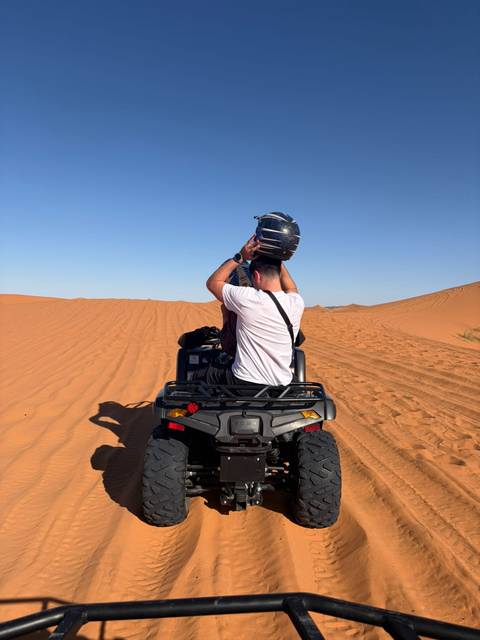       A rider secures his helmet on an ATV parked atop bright orange Sahara sand dunes.
  