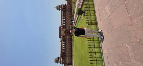       Visitor poses in front of the grand entrance of Agra Fort on a sunny day.
  