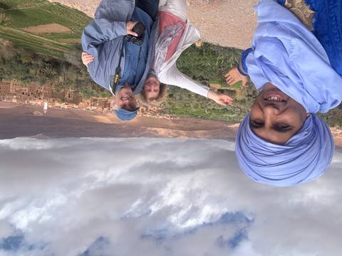       Travellers and their guide celebrate above a lush Moroccan valley dotted with earthen villages and palm groves.
  