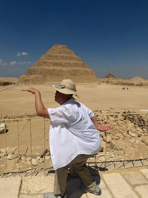       Visitor playfully poses before the Step Pyramid at Saqqara on a bright desert day.
  