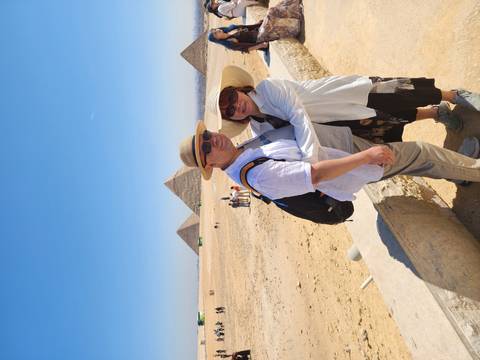       Couple embraces with the Great Pyramids of Giza rising behind them under a clear sky.
  