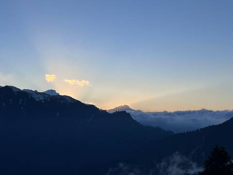       Silhouetted mountain ridge at dusk with the sun dropping behind clouds and a blanket of fog in the valley.
  