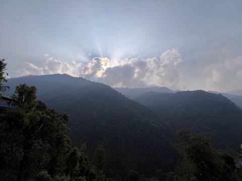       Sunbeams break through dramatic clouds above densely forested ridges in the Himalaya.
  
