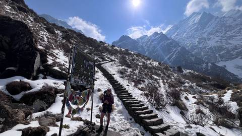       Trekker climbs a snowy stone staircase toward glaciated peaks under bright sun.
  