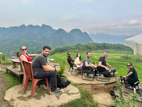       Travellers relax on a wooden deck overlooking emerald rice terraces and misty limestone peaks.
  