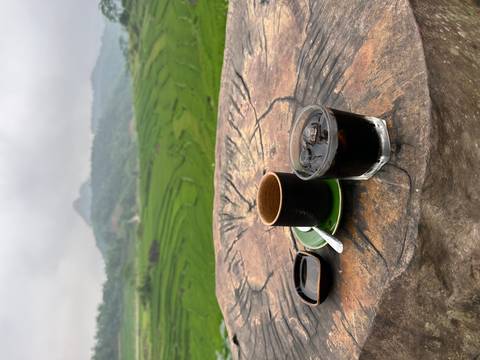       Glasses of Vietnamese coffee sit on a rustic tree-trunk table with sweeping views of layered rice terraces and misty hills.
  