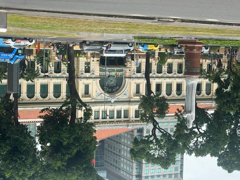       Historic Saigon Central Post Office with clock façade framed by tall trees and city traffic in the foreground.
  