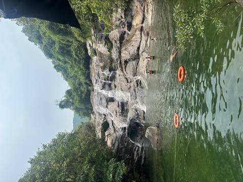       Travellers swim beneath a rocky jungle waterfall spilling into a clear natural pool.
  