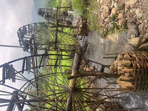       Traditional bamboo water wheels turning in a small stream among lush rice fields and misty hills.
  