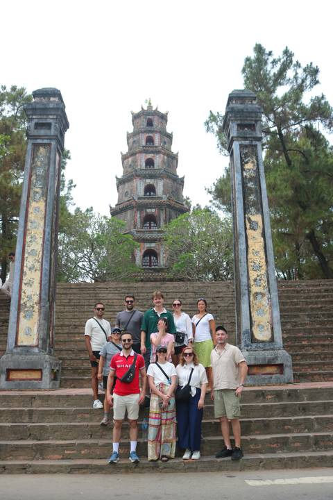       Tour group poses in front of the tall tiered Thien Mu Pagoda framed by ancient stone pillars.
  