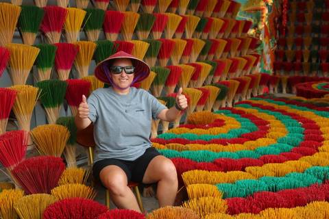       Smiling traveler with thumbs up sits among brightly colored bundles of incense sticks arranged in patterns.
  