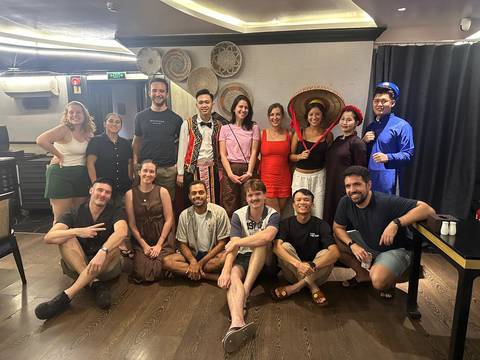       Large tour group gathers indoors wearing traditional and casual outfits for a posed photo.
  