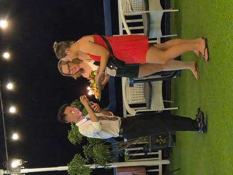       Crew member presents a lit birthday cake to two guests on a boat deck at night.
  