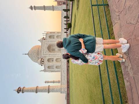       Couple embraces while admiring the Taj Mahal at sunset, standing on manicured lawns.
  