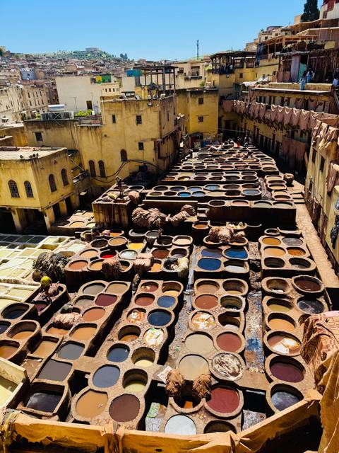       Colorful circular dye vats fill a traditional leather tannery surrounded by yellow adobe buildings in Fes
  