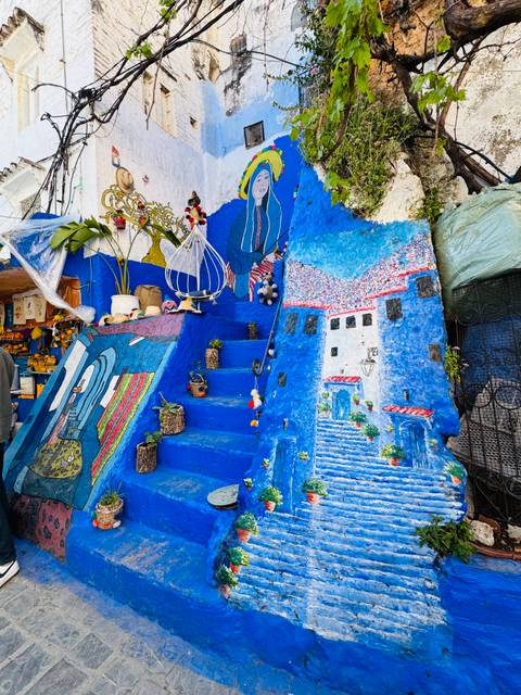       Vibrant blue staircase decorated with plants, paintings and crafts in the medina of Chefchaouen
  