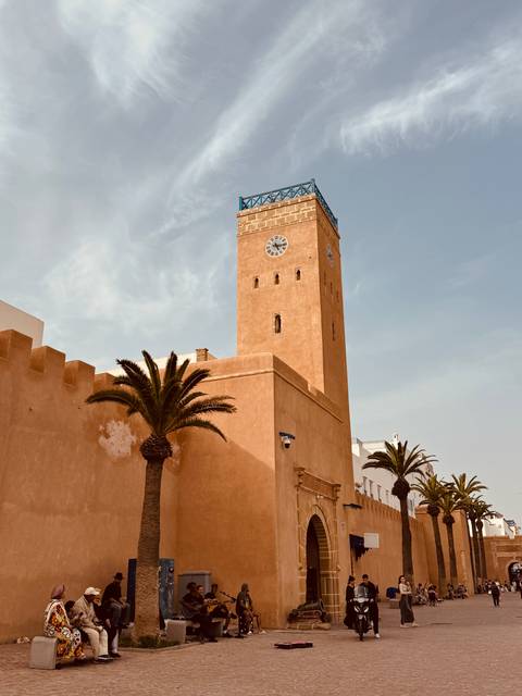       Ochre clock tower and fortress walls framed by palm trees in the coastal town of Essaouira
  