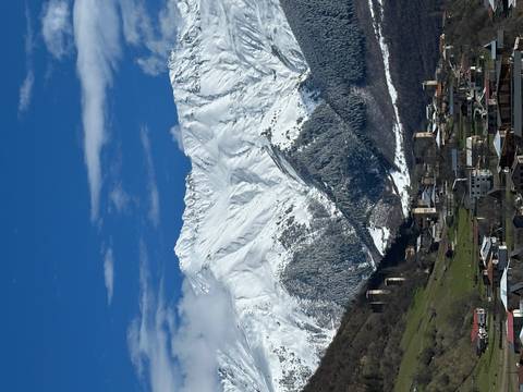       Snow-covered Caucasus mountains tower above a valley village dotted with medieval Svan stone towers under a crisp blue sky.
  