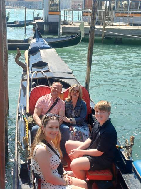       Family seated in a gondola on emerald waters of Venice’s canal with sunlight glinting
  