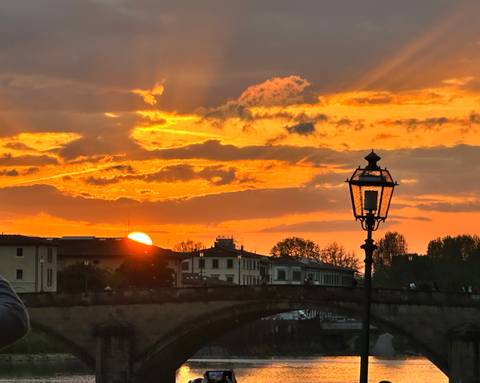       Setting sun over the Arno river with an antique street lamp silhouetted against an orange sky
  