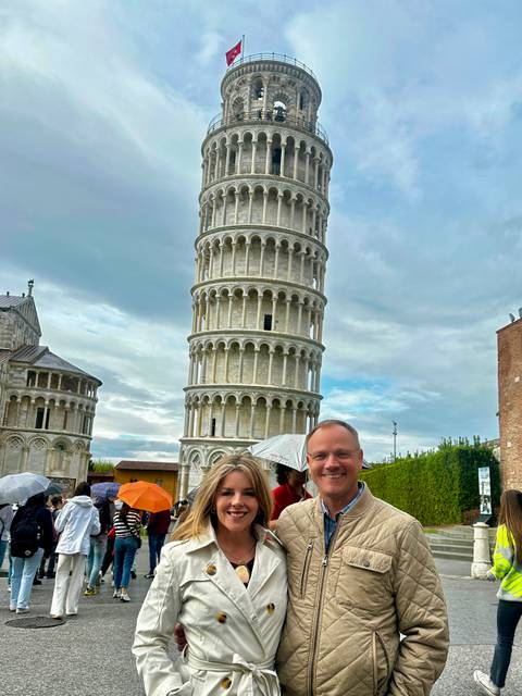       Couple posing with umbrellas in front of the Leaning Tower of Pisa on a cloudy day
  
