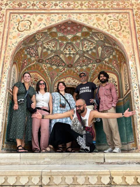       Travelers smile inside an ornately painted Mughal archway filled with floral and geometric patterns.
  