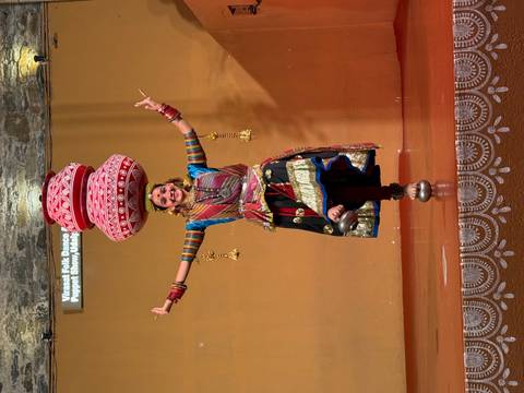       A folk dancer balances stacked clay pots on her head while performing on a stage in traditional Rajasthani costume.
  
