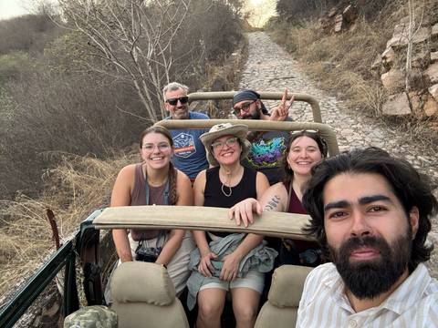       Friends take a cheerful selfie while riding in an open jeep along a rugged cobblestone trail lined with dry brush.
  