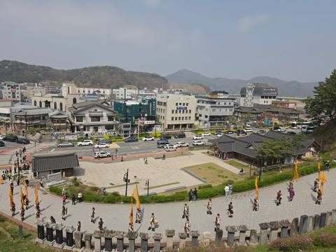       Bustling Korean town center with tiled-roof pavilions, modern shops and pedestrians framed by low mountains.
  