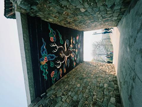       Stone tunnel with vividly painted Korean dragon motif on the ceiling opening onto a sunlit path with visitors.
  