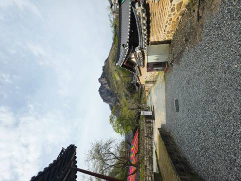       Gravel pathway between traditional Korean walls leading toward a rocky mountain peak under soft clouds.
  