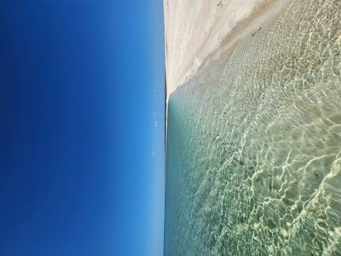       Pristine white sand meets crystal-clear turquoise water under a flawless blue sky on a remote beach.
  