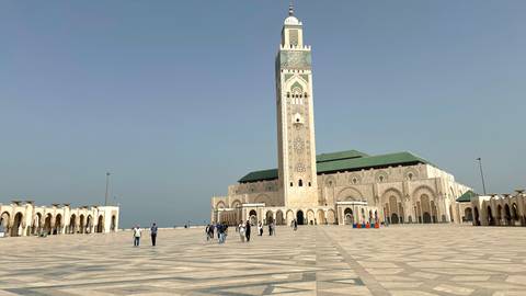       Wide plaza with the towering Hassan II Mosque minaret and visitors walking
  