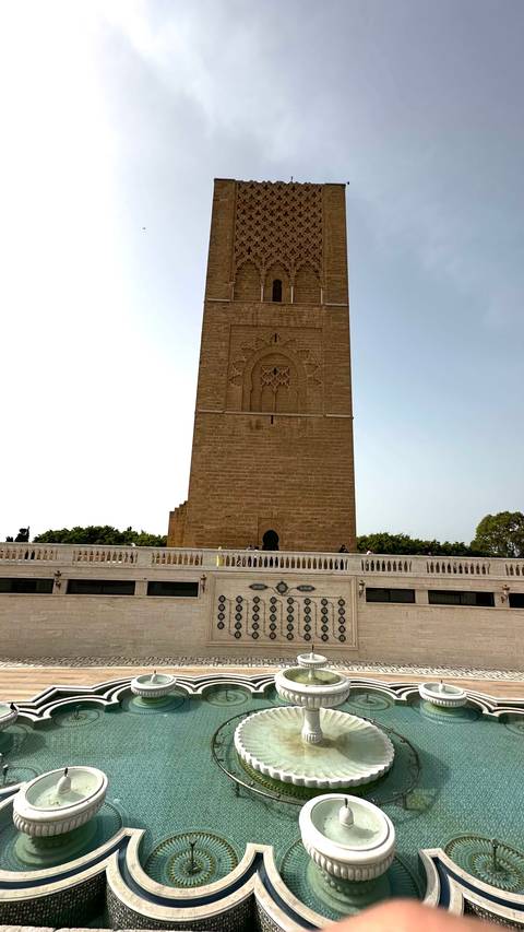       Tall sandstone Hassan Tower rises above a white marble terrace with visitors
  