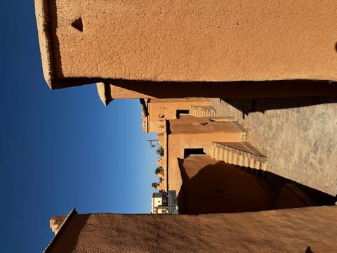       Narrow stone alley between tall ochre kasbah walls under vivid sky
  