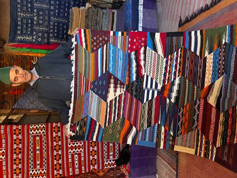       Merchant proudly holds an intricate multicoloured Berber carpet in market
  